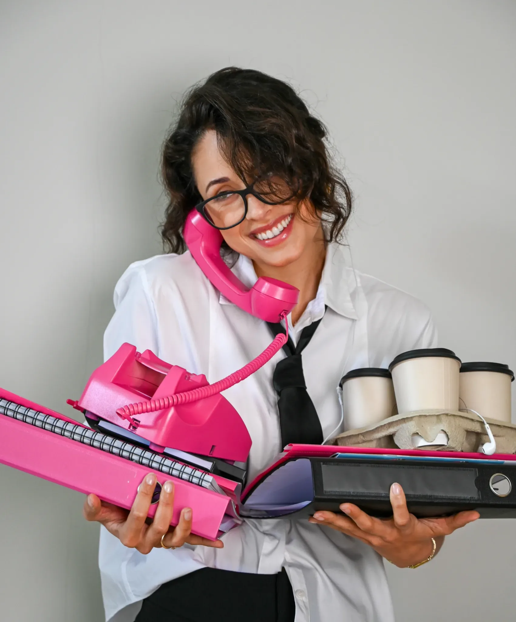 Een assistant die haar handen vol heeft met mappen en belt.